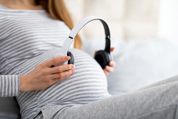 Expecting mother holding headphones over belly, cropped