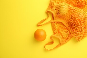 String bag with fresh oranges on yellow background, top view. Space for text