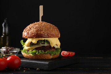 Tasty vegetarian burger, tomatoes and spices on black wooden table. Space for text