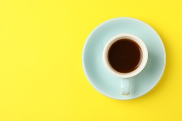 Tasty coffee in cup on yellow background, top view. Space for text