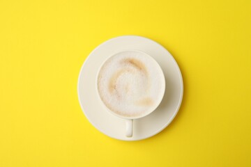 Tasty cappuccino in coffee cup on yellow background, top view