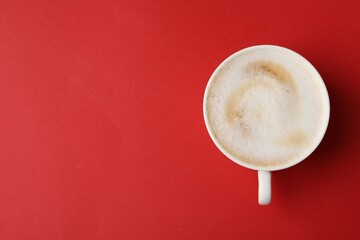 Tasty cappuccino in coffee cup on red background, top view. Space for text
