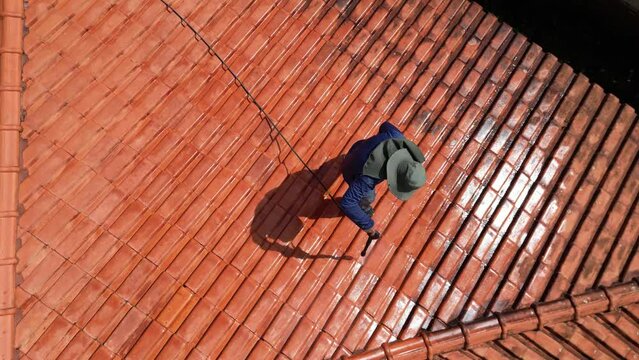 A person outdoors cleaning the red clay roof using a high pressure washer. Professional washing house tiles with water hose.