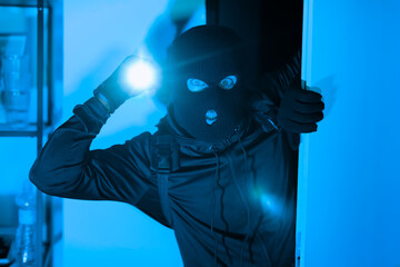 Burglar with flashlight illuminating his face in dark room
