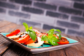 Italian caprese salad with sliced tomatoes, mozzarella, basil, olive oil on wooden background. Top...