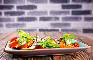Italian caprese salad with sliced tomatoes, mozzarella, basil, olive oil on wooden background. Top view. - 786632741