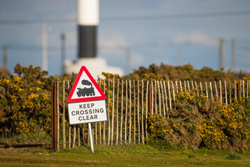 Keep Crossing Clear Railway Sign at Dungenees end of line Romney, Hythe & Dymchurch Railway, Small Sign showing danger steam trains with Lighthouse in background, Sunset evening, with heather, fence