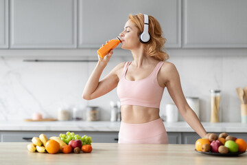 Sport woman snacking on carrot in kitchen