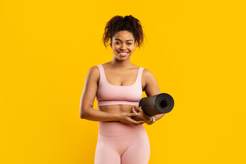 Smiling woman holding yoga mat on yellow