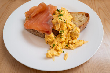 Scrambled eggs sprinkled with chives on sourdough toast with smoked salmon on a white plate. - 786637338