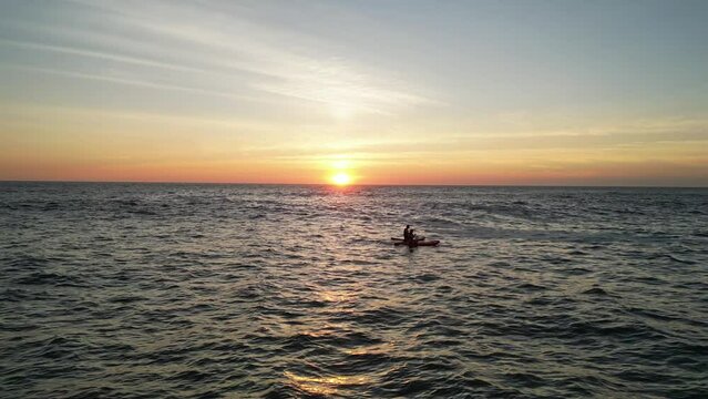Drone shot of two persons kayaking in the sea at sunset time