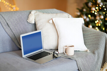 Laptop on sofa in room with festive lights of the Christmas tree