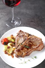 Delicious fried beef meat, vegetables and glass of wine on grey table
