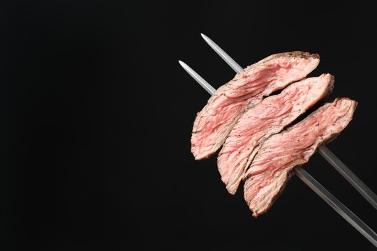 Meat fork with grilled beef pieces on black background, closeup. Space for text
