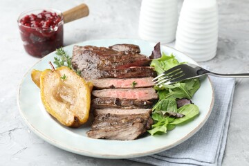 Delicious roasted beef meat, caramelized pear and greens served on light table, closeup