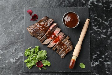 Pieces of delicious roasted beef meat with sauce and greens on black table, top view