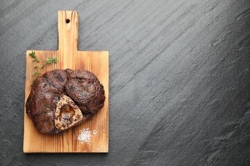 Piece of delicious grilled beef meat, thyme and salt on black table, top view. Space for text