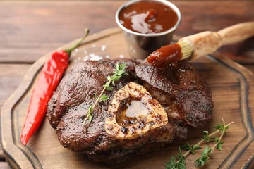 Poster Delicious roasted beef meat served with sauce and spices on wooden table, closeup © New Africa