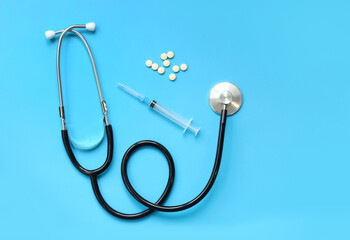 Stethoscope, pills and syringe on a blue background, top view. Cardiology and healthcare concept....