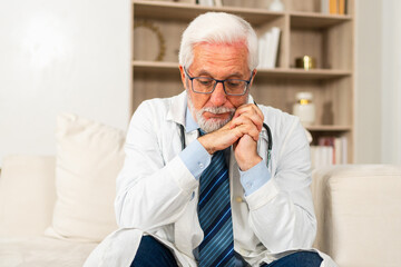 Sad tired mature senior male doctor in medical uniform in hospital or doctor office. Unhappy...