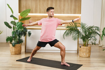A man practices yoga in a peaceful home environment, with green plants adding tranquility to the...