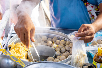 Bakso seller (meat ball seller) serves for customers in a stall cart. Bakso is one of indonesian...
