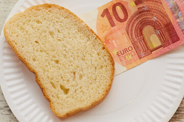 A 10 euro bill and bread lie on a plate, bread and euro on a plate, bread and money on a plate, close-up