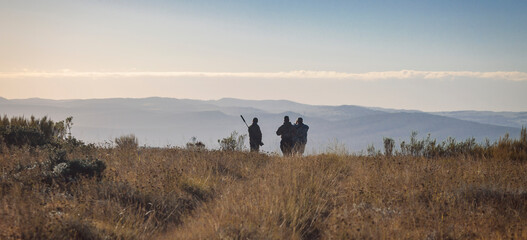 Hunter, huntsman and tracker inspect the mountainous terrain in search of animals.