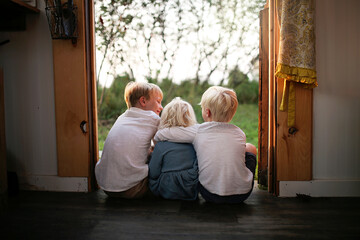Three happy Little Kids are Sitting in Country Cottage Doorway Hugging each Other