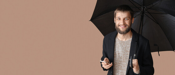 Handsome man with umbrella and mobile phone on color background
