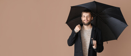Handsome man with umbrella on color background