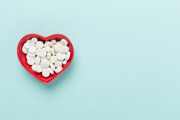 Medicines in heart-shaped bowl on color background, top view