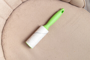 Sticky roller for clothes on beige armchair. Hair and animal hair on furniture. Furniture cleaning. Space for text