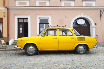 Historical district of city. Vintage yellow car against background of old house. Cozy atmosphere of old street.