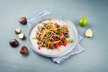 Traditional Asian wok spinach with chestnuts, pepper strips and soy sprouts served as close-up in a Nordic design plate with copy space