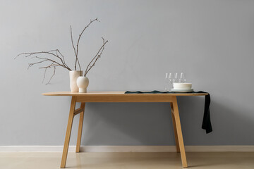 Clean tableware and vases with tree branches on wooden table near light wall