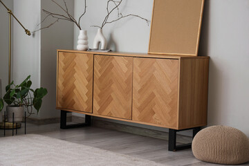Wooden sideboard with vases and blank frame near grey wall in living room