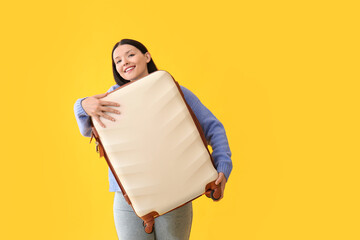 Beautiful young woman holding suitcase on yellow background
