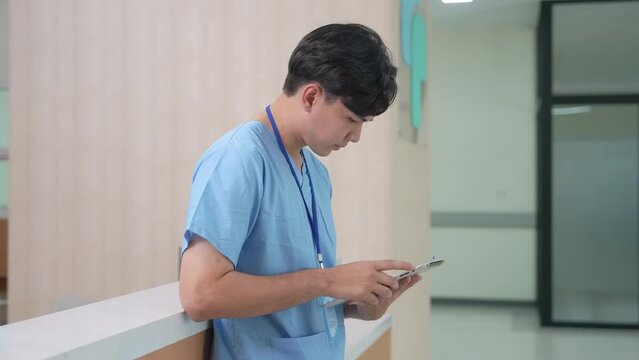 Young physician assistant man diagnose patient symptoms using technology tablet or reading prescriptions for medical therapy, Asian doctor trainee in blue uniform attention to health care information