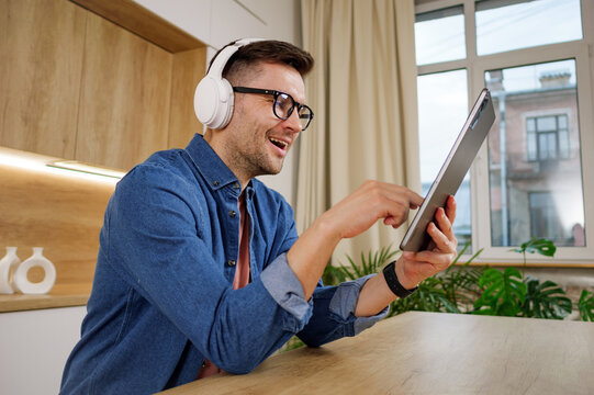 An exuberant young man interacts with a tablet, headphones on, in a well-lit office with minimalist decor.