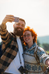A beautiful and cheerful hiking couple captures a selfie with a stunning landscape in the background - 786667116