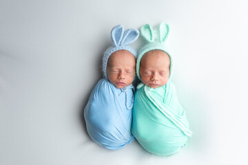 Tiny newborn twins boys in white cocoons on a white background. A newborn twin sleeps next to his brother. Newborn two twins boys hugging each other.Professional studio photography