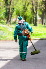 Worker in green uniform with a grass trimmer
