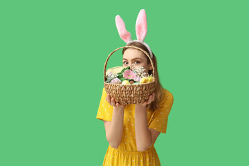 Young woman in bunny ears headband holding basket with makeup products, flowers and Easter decor on...