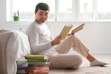 Young man with books sitting in bedroom