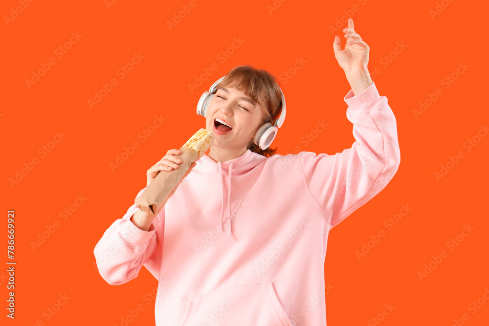 Sticker Young woman in headphones with doner kebab on orange background