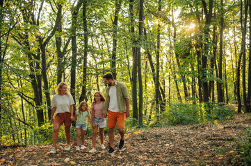 Fototapeta premium A happy family is holding hands in forest and exploring nature.