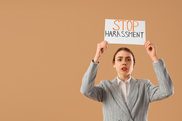 Young businesswoman holding paper with text STOP HARASSMENT on beige background