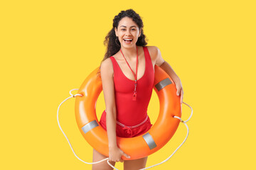 Beautiful young happy African-American female lifeguard with ring buoy on yellow background