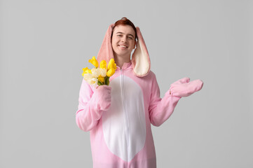 Happy young man in Easter bunny costume with flowers pointing at something on white background